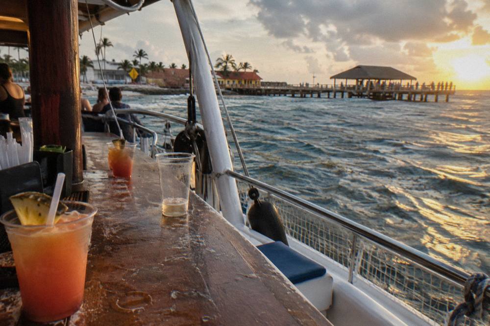 Open deck of a catamaran with drinks on the bar counter as the sun sets over calm sea