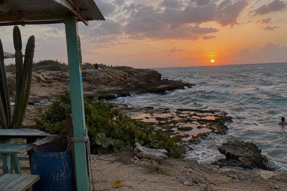 A quiet beach at dusk with the sun low over calm sea and a few clouds catching orange light