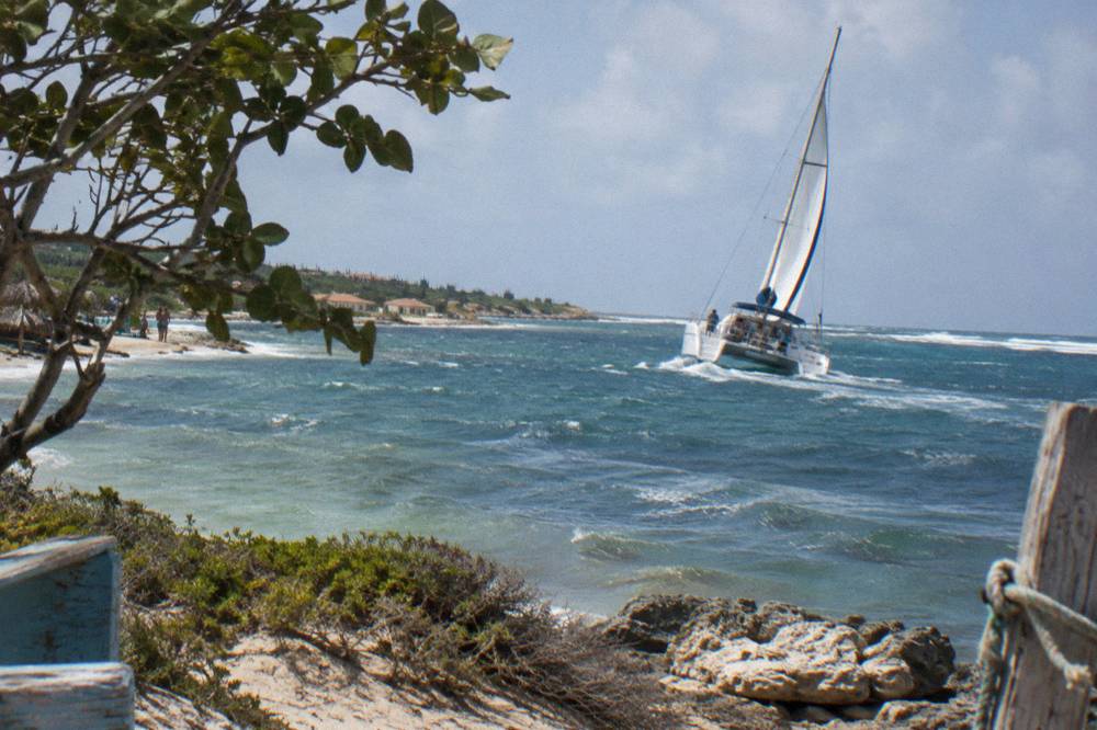 A sailing catamaran heeling slightly in steady wind on open blue water near an island coast