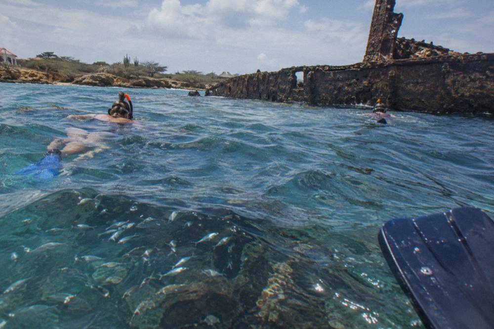 Snorkelers in the water beside the hull of a sunken ship with fish above the reef at late afternoon