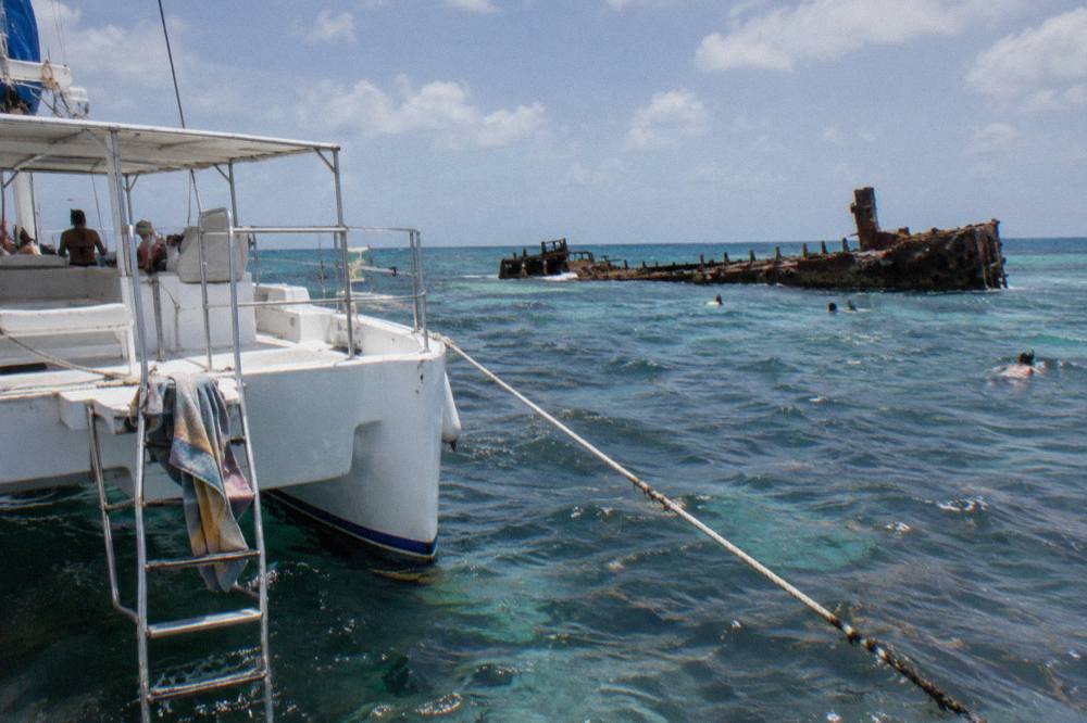 A snorkel boat anchored near a long dark wreck hull in clear blue water