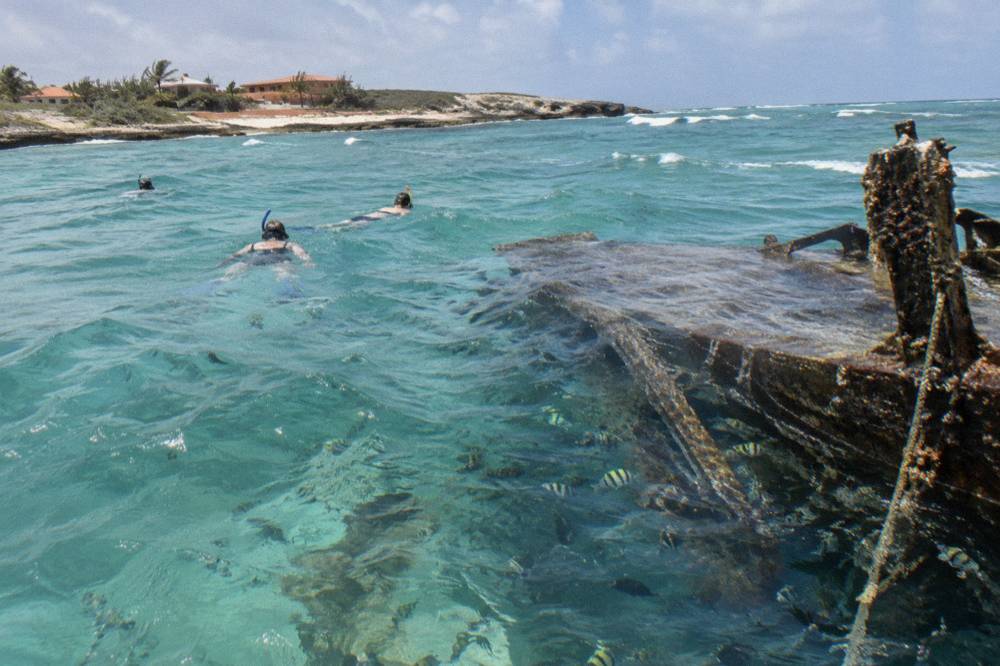 Snorkelers floating in clear water above a sunken hull with fish around it