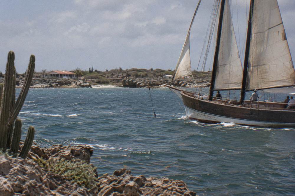 A wooden schooner under sail near the Aruba coast in late afternoon light