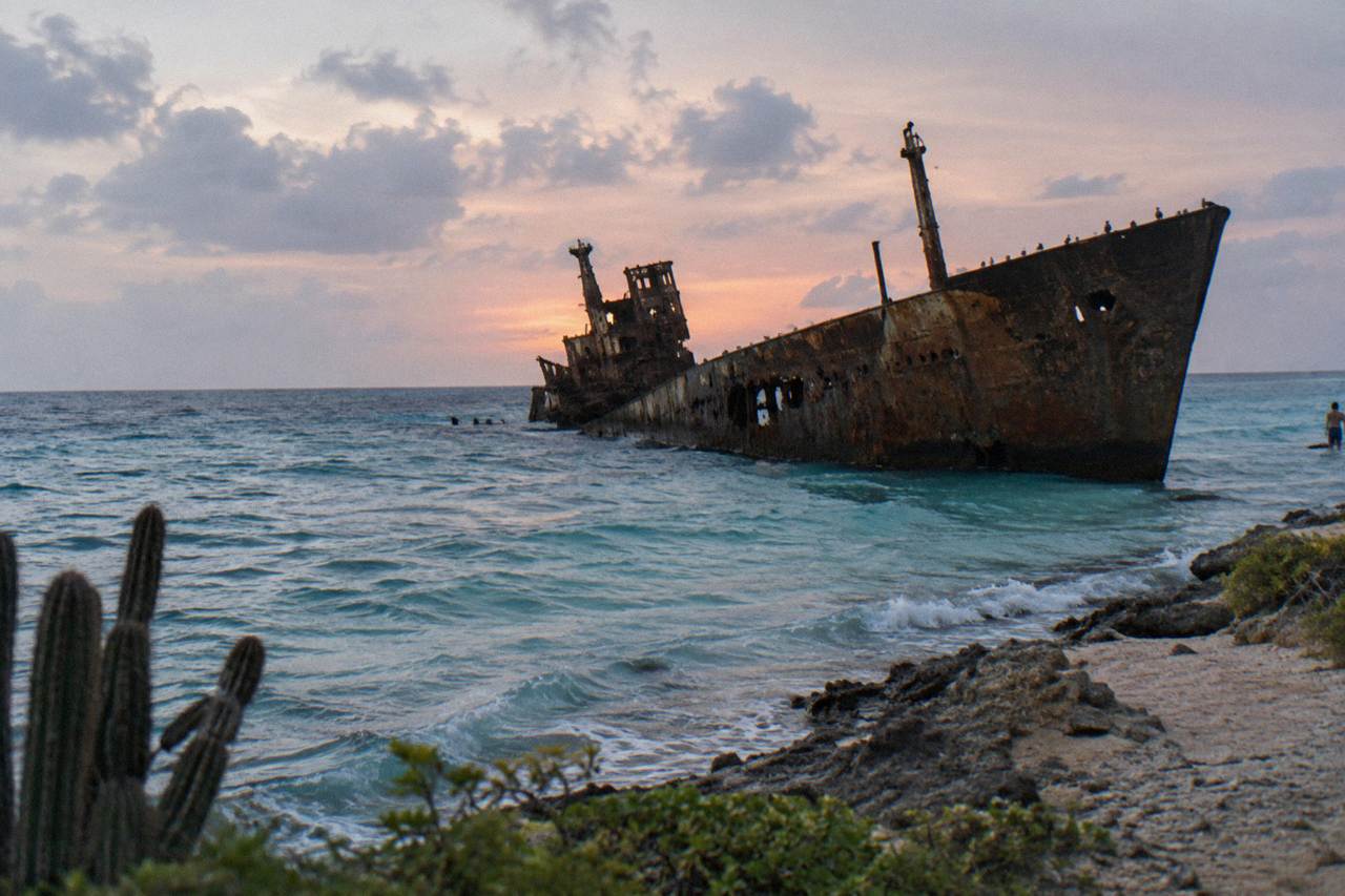 A dark shipwreck hull rising above calm turquoise water near the Aruba coast at dusk