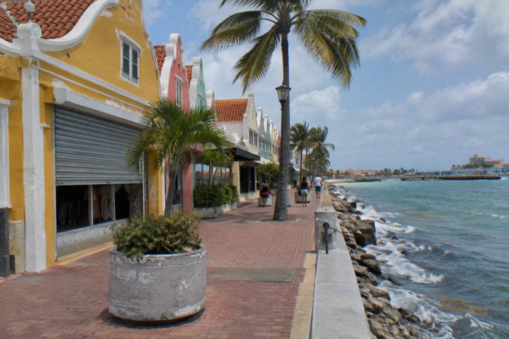 Colorful Dutch colonial storefronts along a clean waterfront street in Oranjestad under a blue sky