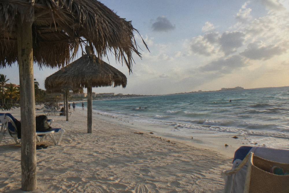 Row of beach palapas along a wide stretch of white sand under an evening sky