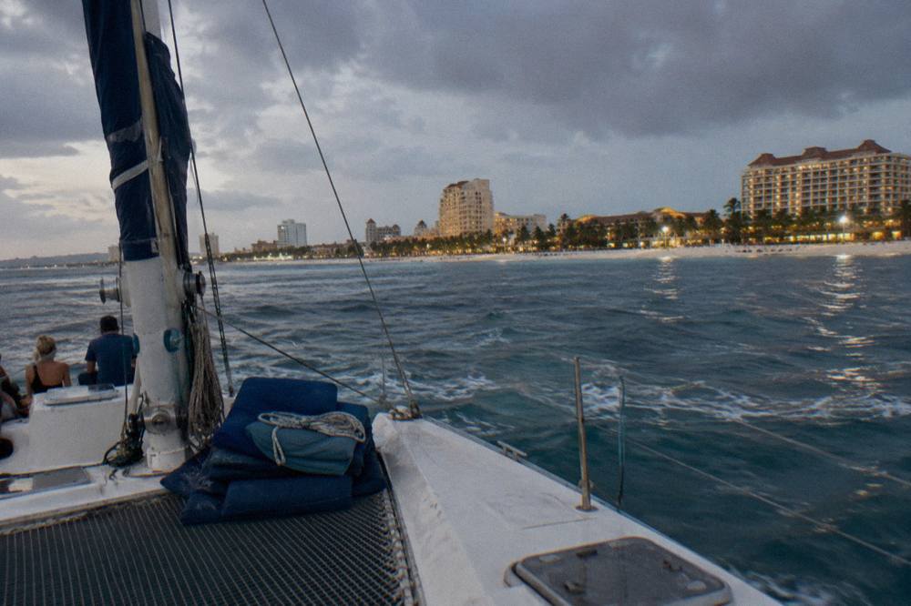 Open deck catamaran cruising along the Palm Beach coastline under a darkening evening sky