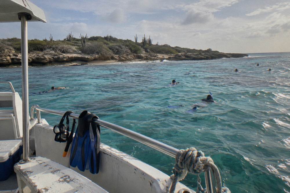 Passenger boat anchored near a shallow reef with snorkelers in calm turquoise water before sunset