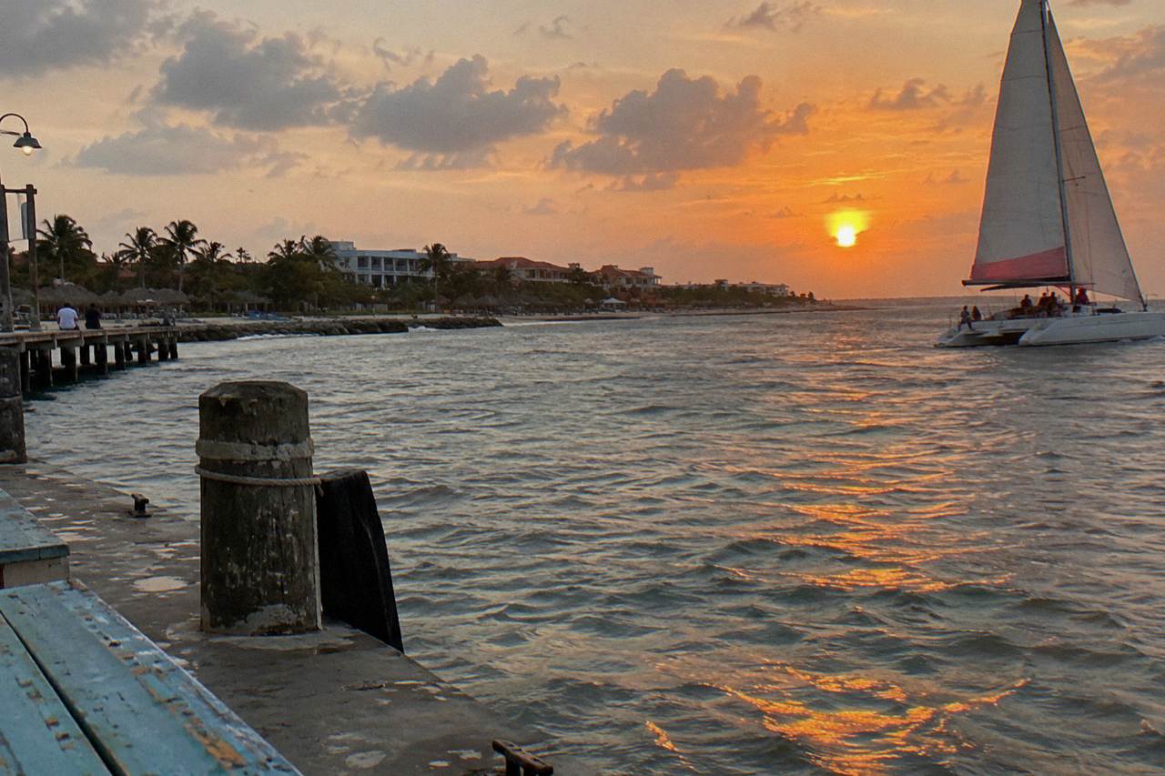 Catamaran under sail on calm water as the sky turns orange over the Caribbean sea near Aruba