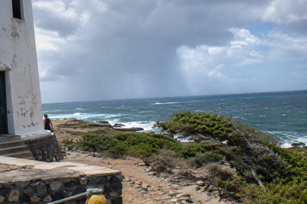 A rain shower passing over open sea with a band of clear sky on the horizon