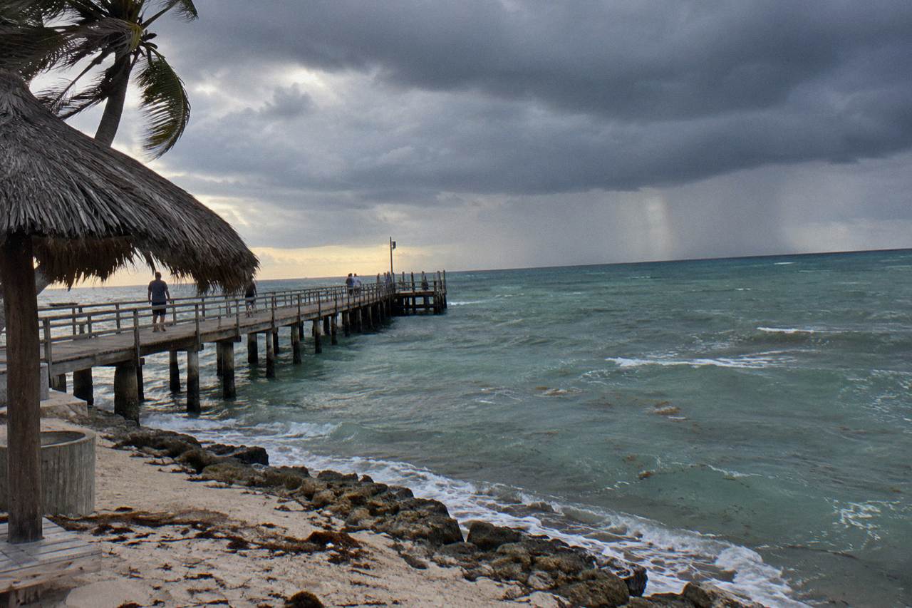 Dark rain clouds gathering over calm Caribbean water near a wooden pier at dusk