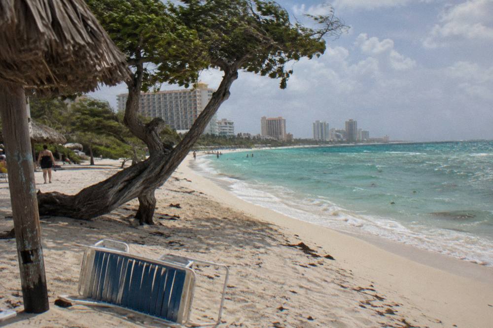 Wide sandy beach with calm turquoise water and a row of high-rise resort towers along the shore
