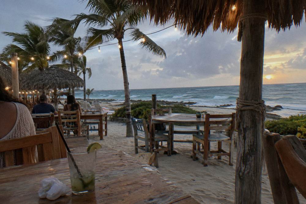 Beachfront restaurant terrace with string lights glowing above tables near the water at dusk