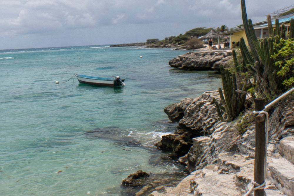 Calm turquoise bay with gentle ripples and a moored small boat near a rocky point