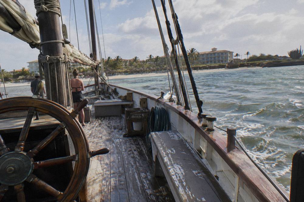 Wooden deck of a pirate schooner with rigging, benches and a steering wheel in late afternoon light
