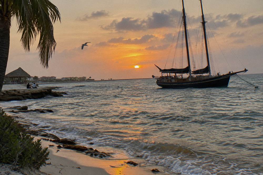 Schooner at anchor seen from the water with orange sky and calm sea at sunset