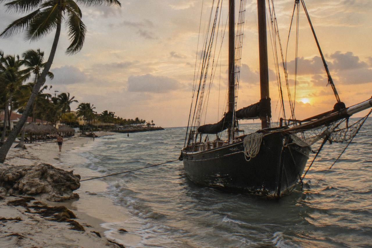 Wooden pirate-style schooner with tall masts moored beside a palm-lined beach at dusk