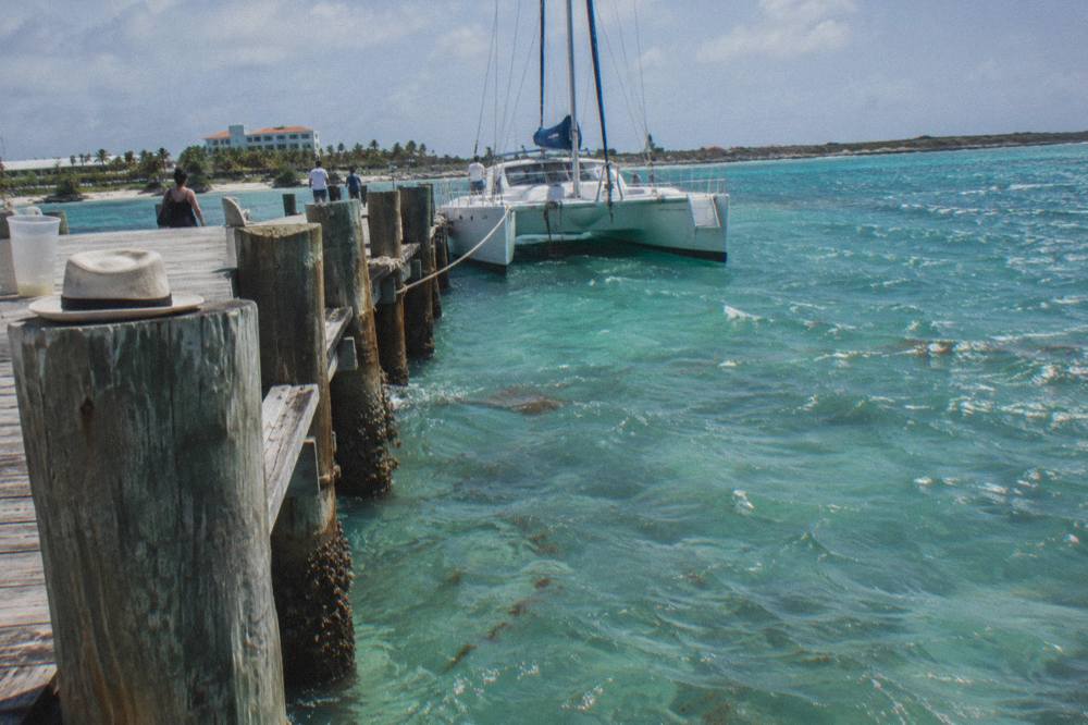 Wooden pier extending into calm turquoise water with a moored sailing boat in late afternoon light