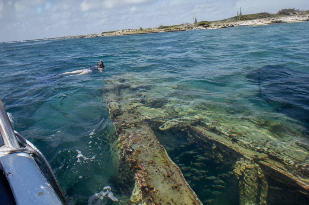 Snorkeler floating above a shallow shipwreck in clear blue water near a reef