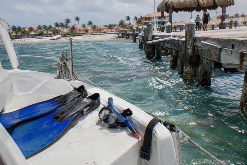 Snorkel fins and mask resting on a boat deck near clear shallow water