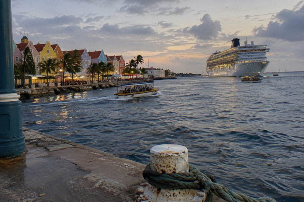 A cruise ship anchored off Oranjestad with small boats crossing the harbor at dusk.