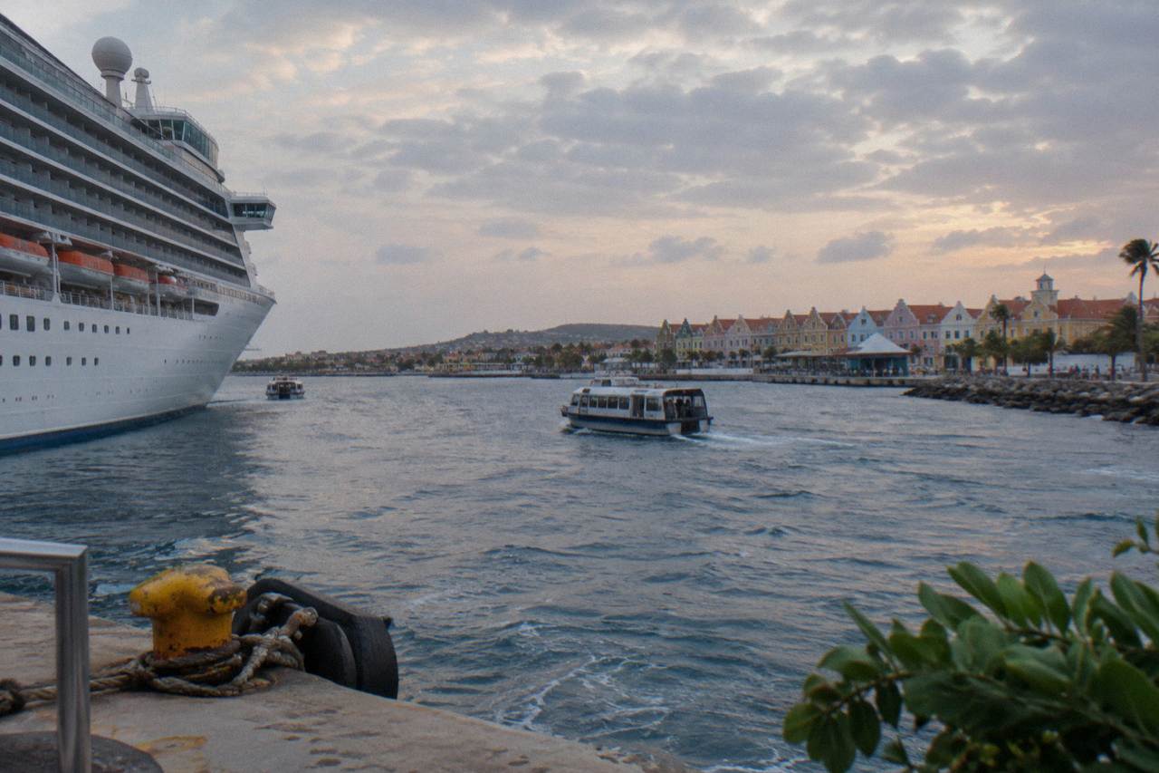 A cruise ship at anchor off the Aruba coastline under a wide evening sky.