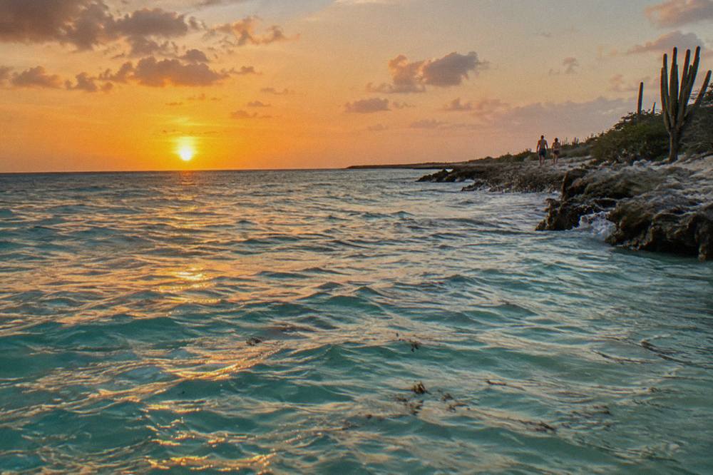 Sun sinking toward the Caribbean horizon with orange sky above calm water