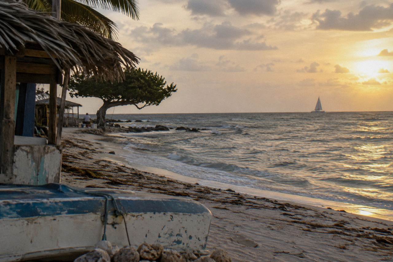 Warm evening light over calm Caribbean water with a distant sail silhouette