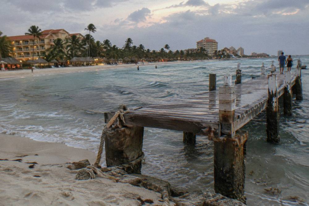 Wooden pier extending over calm evening water with hotel lights glowing along the shore