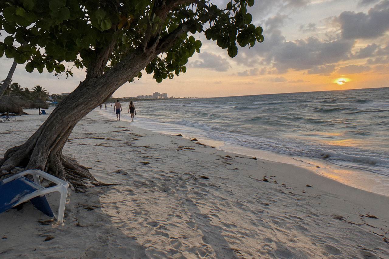 Wide sandy beach in Aruba at dusk with calm water and a dimming orange sky above the horizon