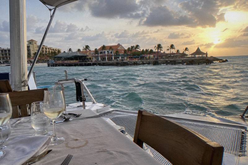 Dinner tables set on the deck of a catamaran off Aruba at golden hour