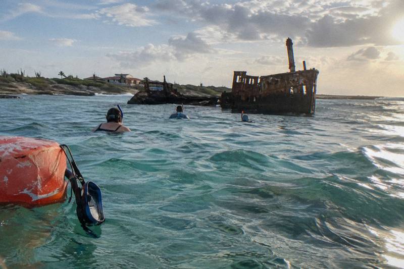 Snorkelers in turquoise shallows near a shipwreck off Aruba in late afternoon light