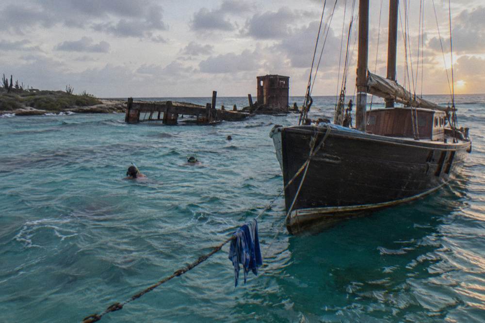 Classic wooden schooner at anchor near a reef with snorkelers in the water at dusk