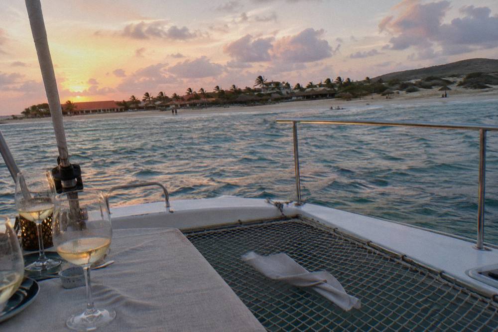 Dinner table set on a catamaran deck with wine glasses at sunset