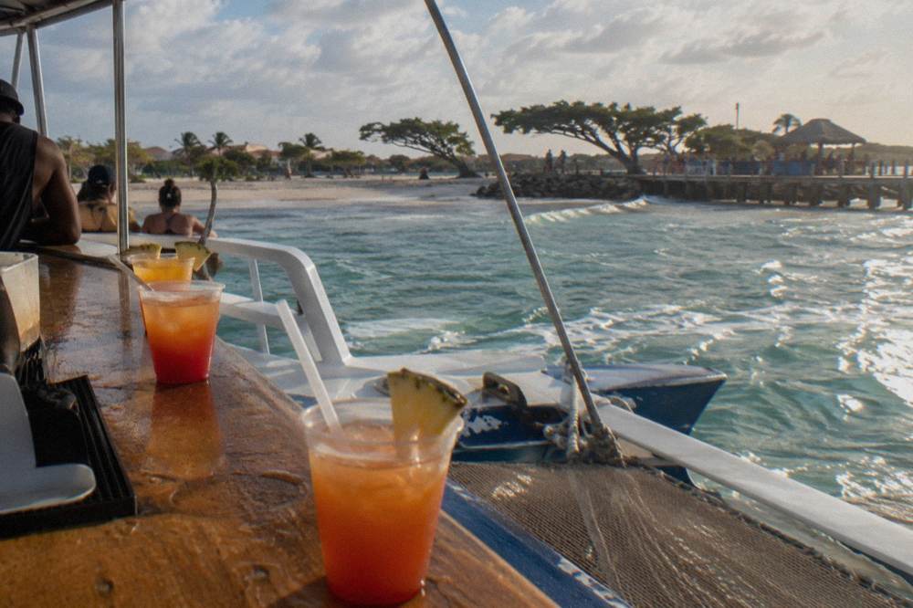 Open-air bar counter on a catamaran deck with drinks lined up at sunset