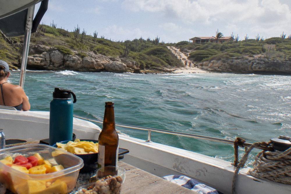A deck table set with drinks and snacks aboard a boat at anchor near the Aruba shoreline