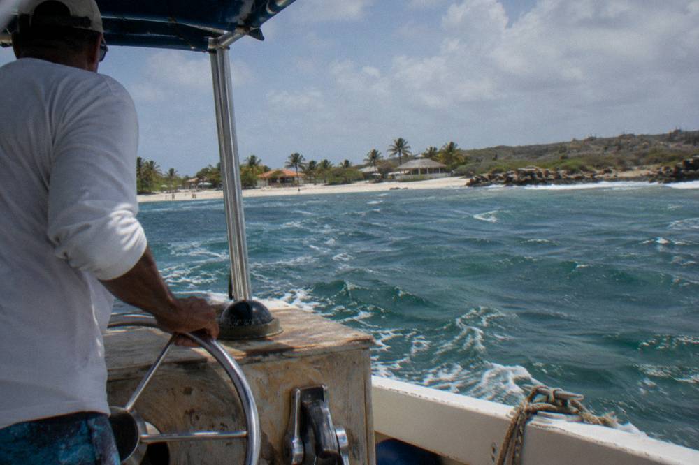 A captain at the helm of a small boat steering toward open water off the Aruba coast