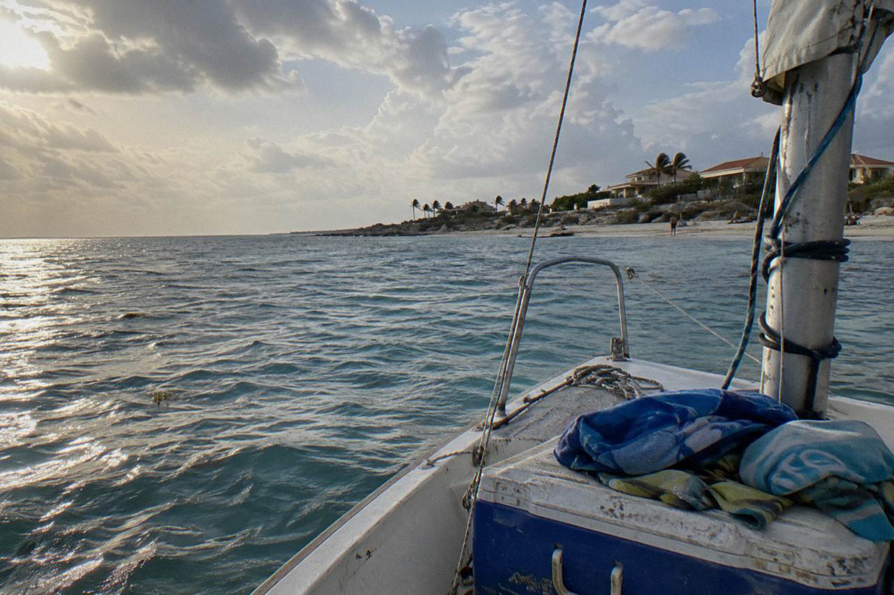 A private sailing boat anchored off the Aruba coast under a partly cloudy sky near sunset