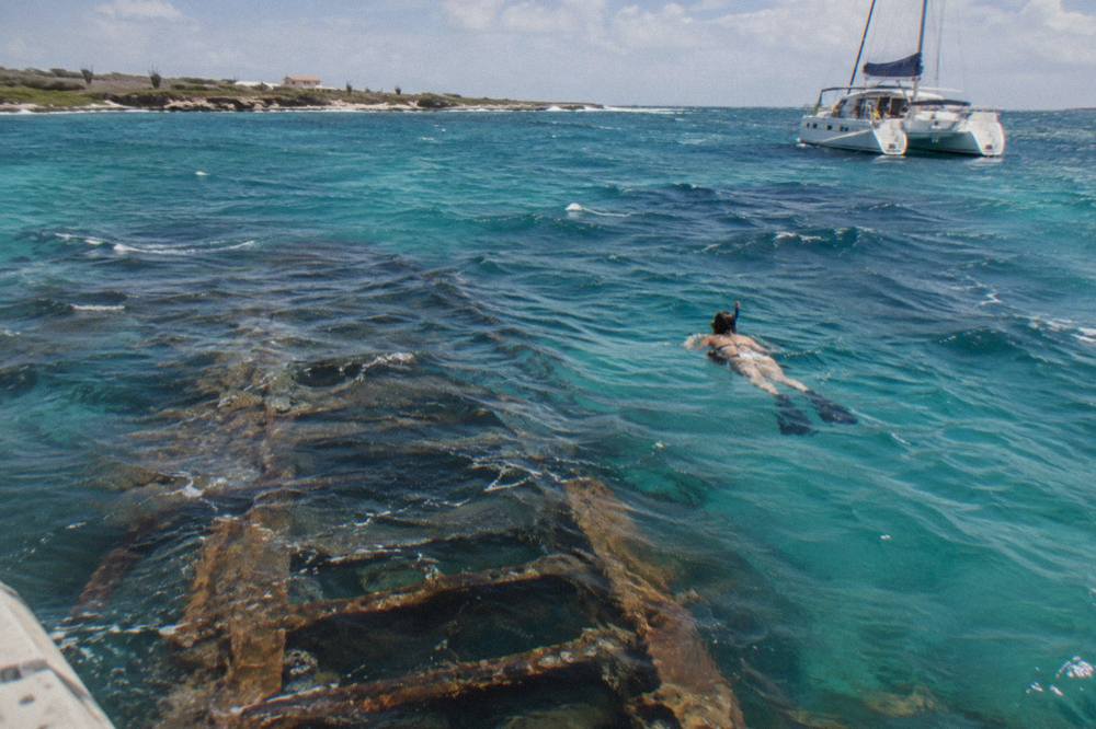 A snorkeler floating above a sunken shipwreck in clear blue water