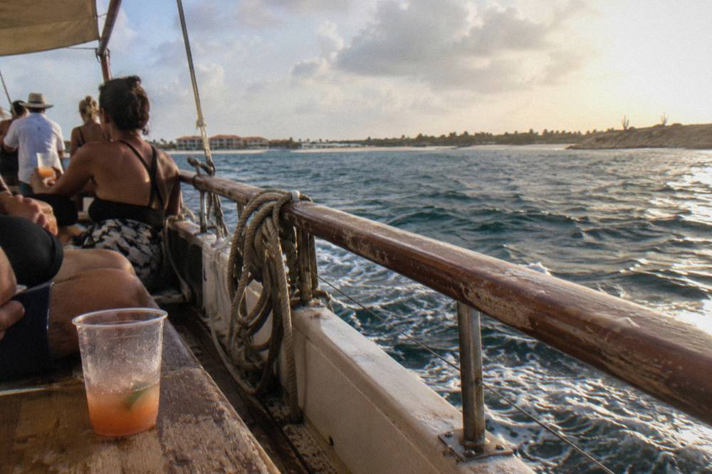 Passengers on a boat deck holding drinks with the sea at sunset