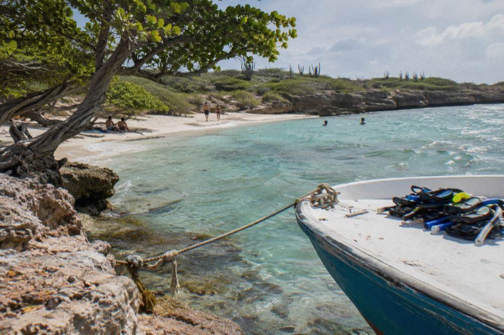 A small tour boat tied up at a rocky cove beside a beach, with snorkel gear on board