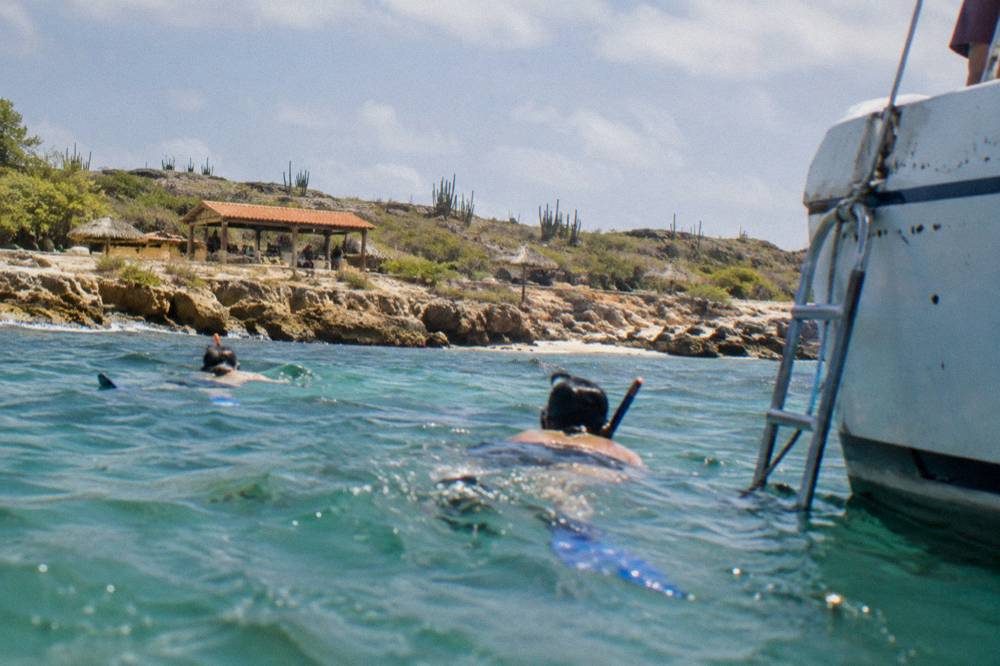 Snorkelers in the water beside a boat ladder in clear shallow water
