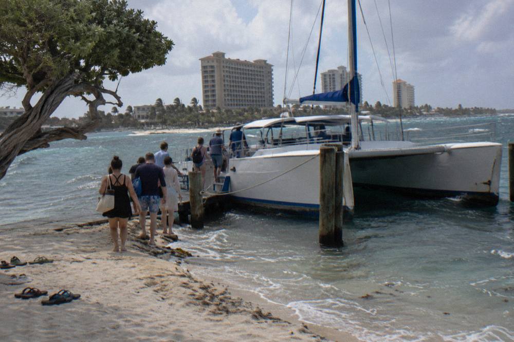 A catamaran moored at a wooden pier on Palm Beach with resort towers behind it in late afternoon light