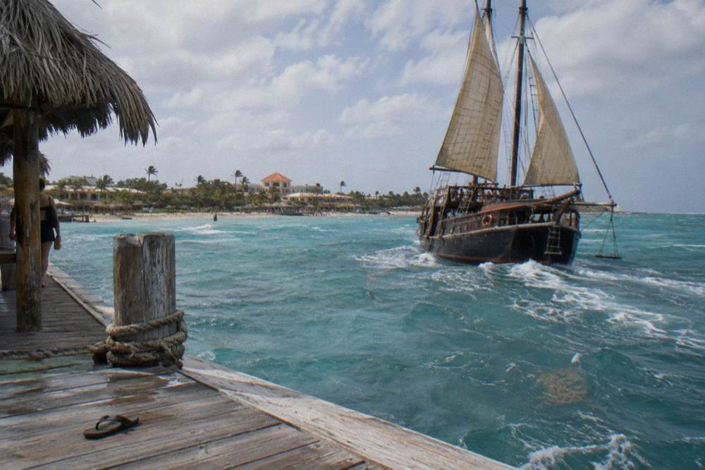 A pirate-style schooner with tan sails and a rope swing motoring away from a Palm Beach pier