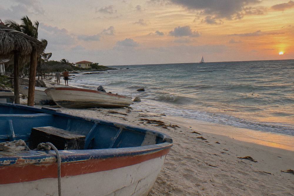 Orange and pink sky over calm Caribbean water near the Aruba coast at dusk with a distant sailboat silhouette