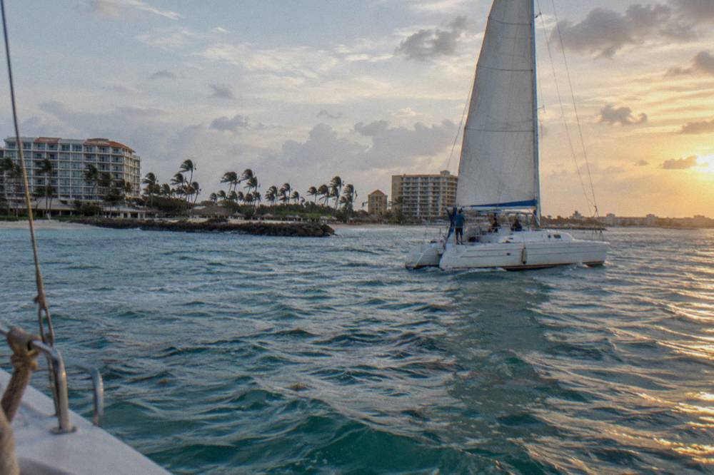Catamaran under sail off Palm Beach in late afternoon light with calm sea and resort towers along the shore