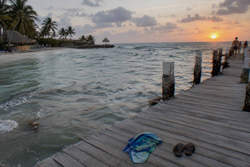 Wooden pier extending over calm evening water toward a low orange sun