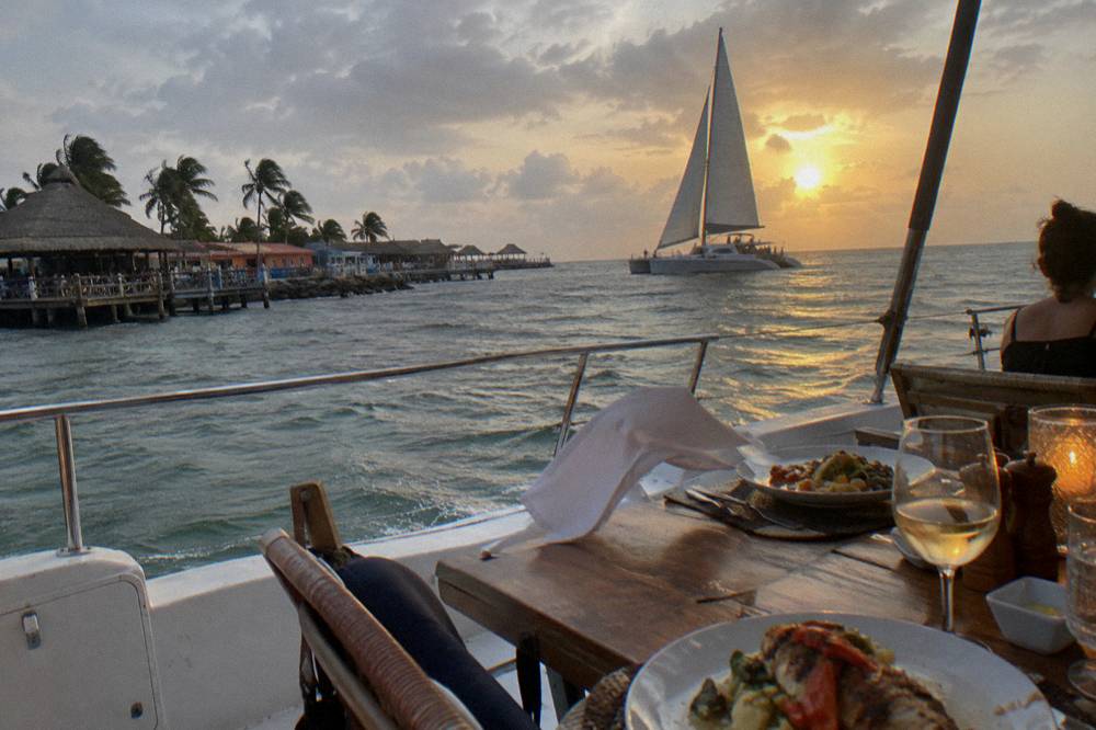 Catamaran under sail on calm golden water with the sun low on the horizon