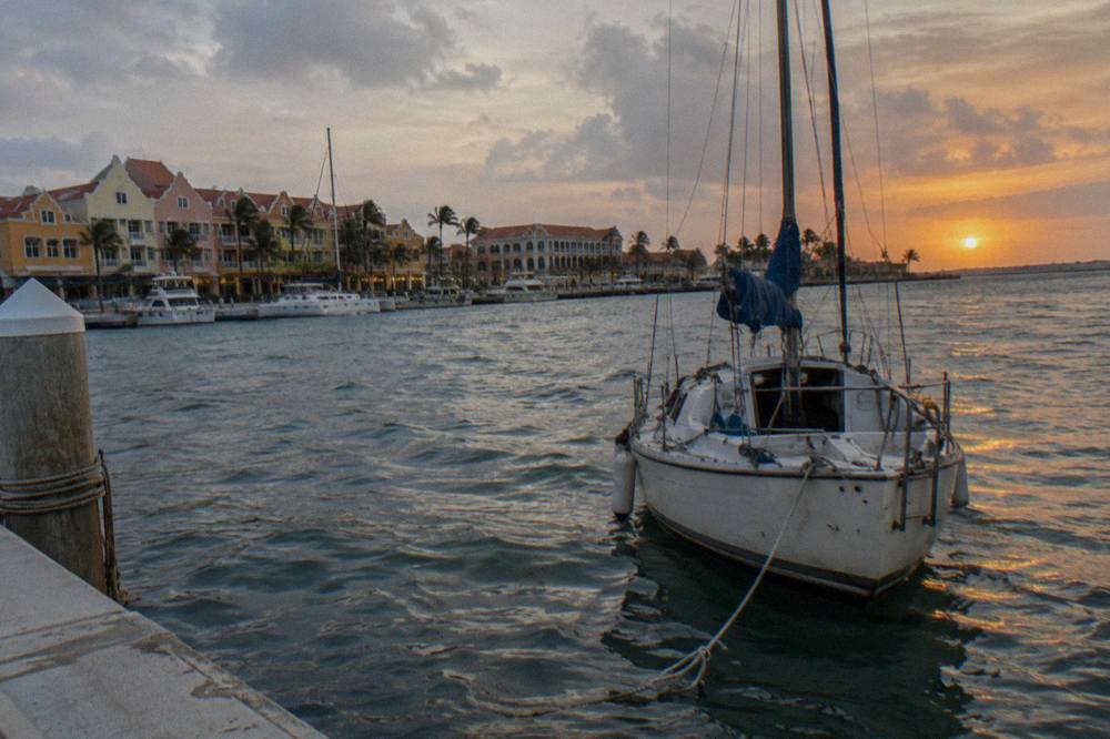 A sailboat on calm Caribbean water as the sky turns orange near the horizon