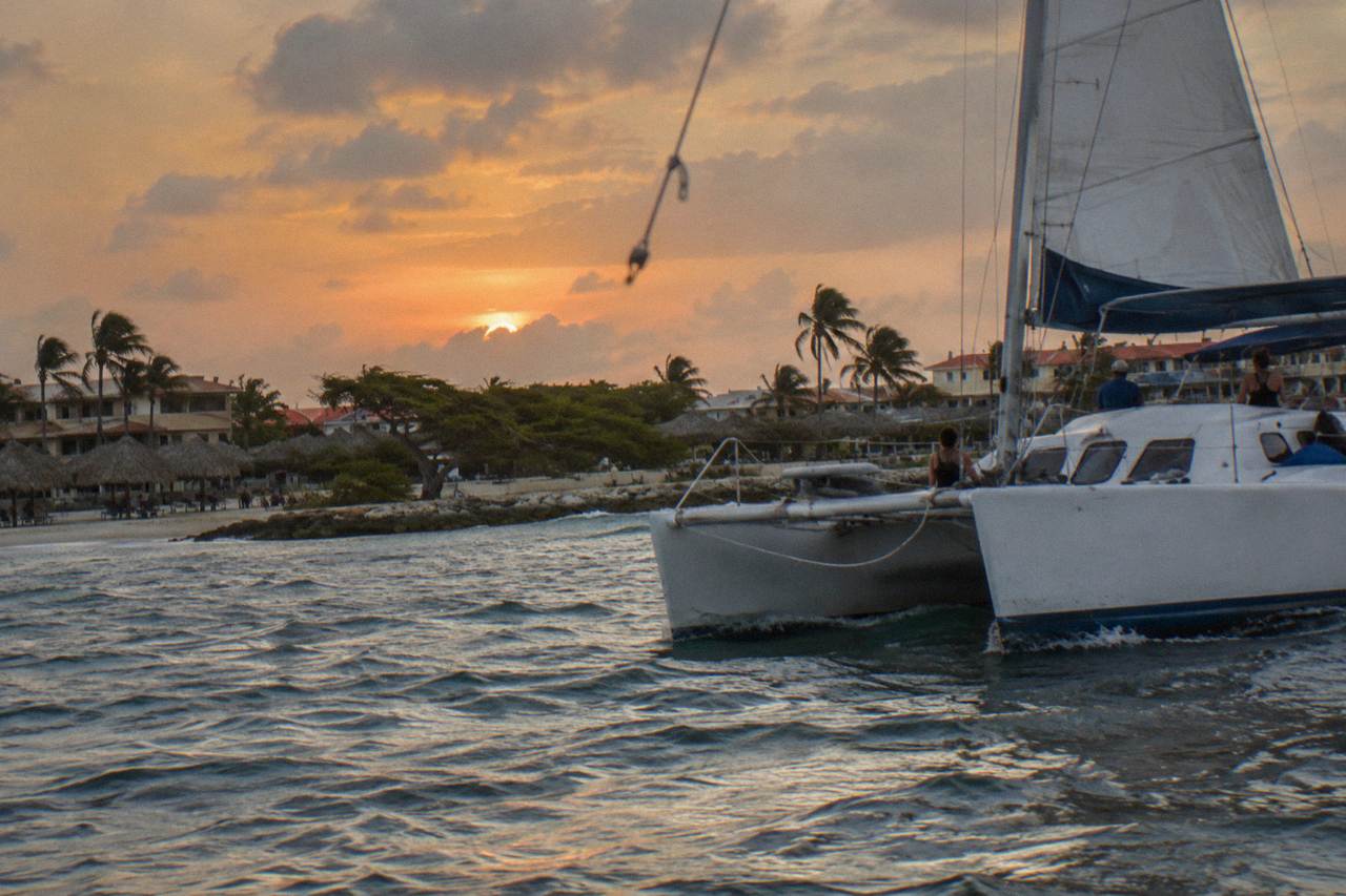 A catamaran under sail off a Caribbean beach at dusk